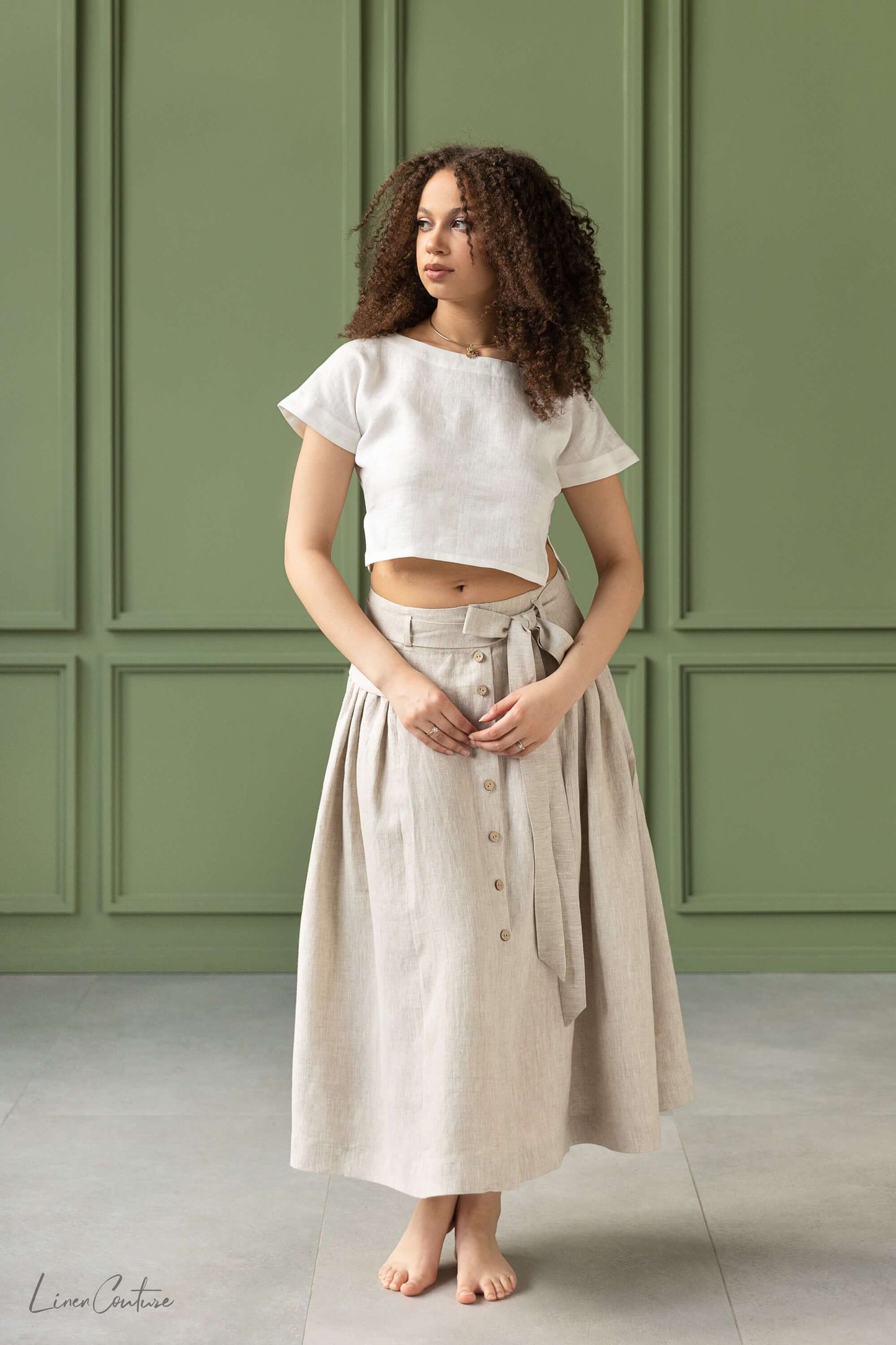 Taormina Set | Linen Crop Top and Flared Midi Skirt modeled by a woman with curly hair in a minimalist setting.