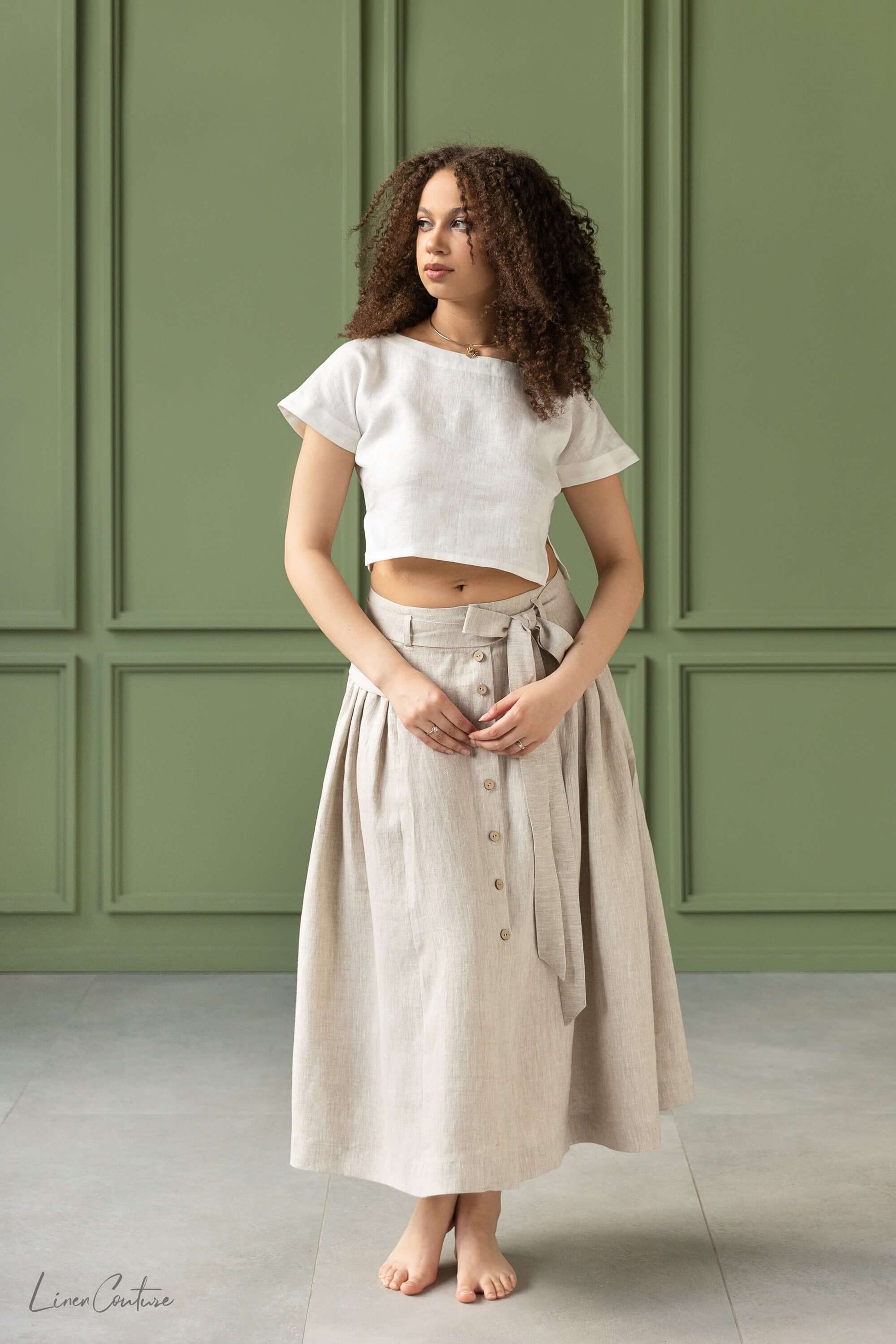 Taormina Set | Linen Crop Top and Flared Midi Skirt modeled by a woman with curly hair in a minimalist setting.