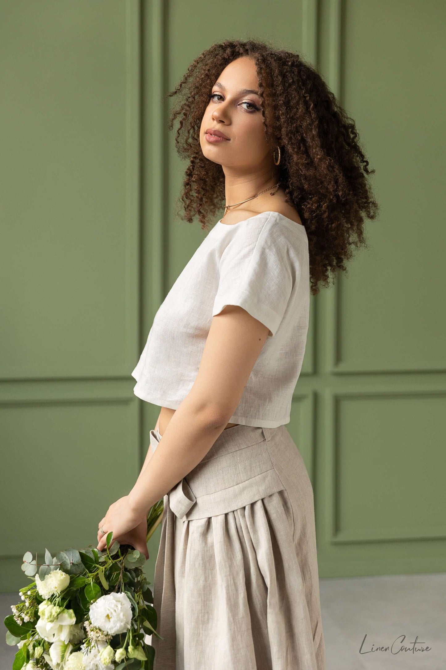 Taormina Set | Linen Crop Top and Flared Midi Skirt in earthy beige worn by a model holding flowers.